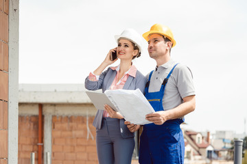 Project developer and construction worker on site using technology like phone and tablet computer