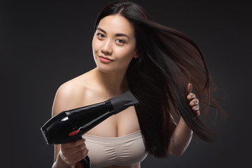 portrait of beautiful asian woman with hair dryer isolated on black - obrazy, fototapety, plakaty