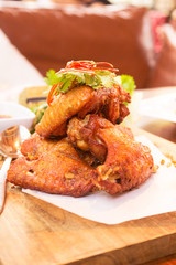 Fried chicken wings on wooden plate with sweet sauce, vertical side view.