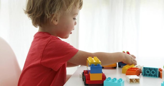Close up of child's hands playing with colorful plastic bricks at the table. Toddler having fun and building out of bright constructor bricks. Early learning. stripe background. Developing toys