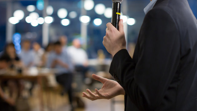 Lecturer at Conference Hall Meeting Presenting Business Marketing Idea Plan. Presenter with Hand Held Up During Presentation to Audience. Business Lecture Speaker on Stage. Teacher Speech. Elections