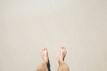 Male bare feet stand on white coastal sand
