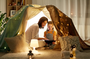 family, hygge and technology concept - happy mother and little daughter with tablet pc computer in kids tent at night at home © Syda Productions