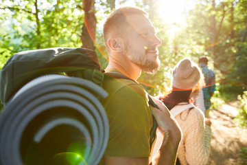 One of young campers with backpack enjoying walk in the forest with his friends walking ahead