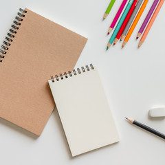 open blank spiral notebook with pencil, eraser and color pencil on white background.