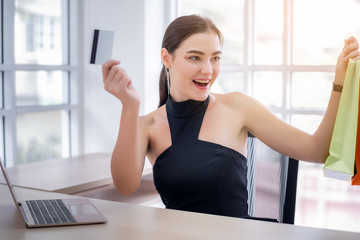 Attractive young businesswoman enjoy shopping online with full of bags with laptop and credit card at office. Have a colorful shopping bags hold on hand. 
