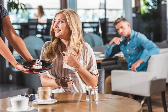 cropped image of waiter showing dessert with flower to surprised woman in cafe
