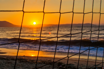 Fototapeta premium View of the sunrise through the volleyball net. Early morning , dramatic sunrise over sea and mountain.