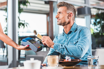 side view of handsome man paying with credit card in cafe