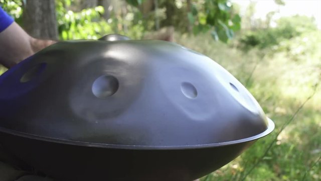 Musician hands playing handpan drum in nature scene.
