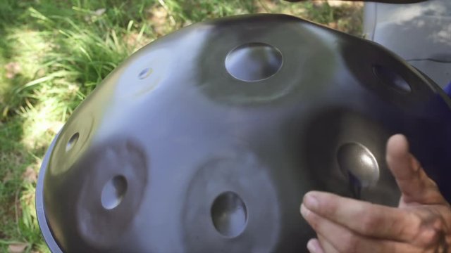 Musician hands playing handpan drum in nature scene.