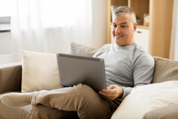 technology, people and lifestyle concept - man with laptop computer sitting on sofa at home