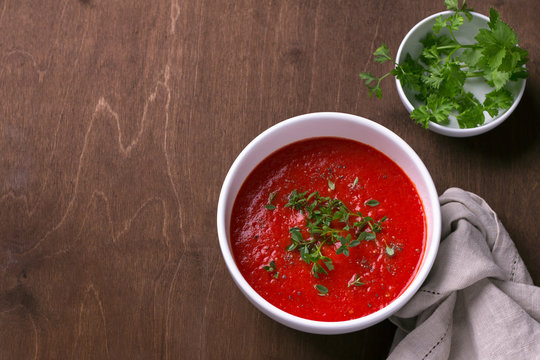 Delicious vegan soup of baked tomatoes and sweet peppers with herbs in a white plate on a wooden background, top view, free space, horizontal