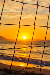 Fototapeta premium View of the sunrise through the volleyball net. Early morning , dramatic sunrise over sea and mountain.