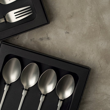 Top view of silver collection of knives forks spoons tablespoons and teaspoons in a black box on a gray concrete background