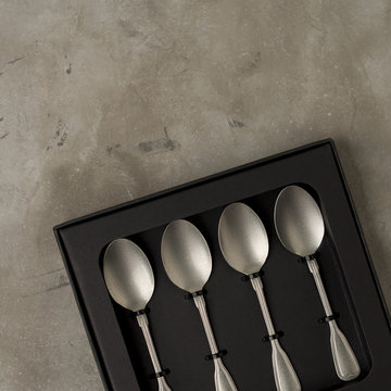 Top view of silver collection of tablespoons teaspoons in a black box on a gray concrete background