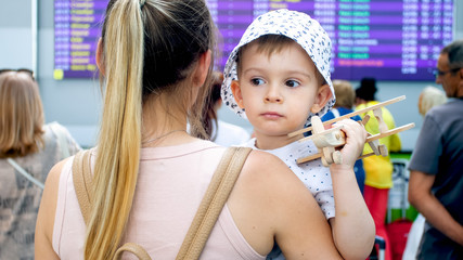 Portrait of young woman hugging her toddler son at big screen with flight departure time in airport