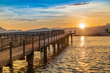 Fototapeta premium Dramatic sunrise during the Fall Equinox over the historical holzsteg pedestrian bridge crossinhg the Upper Zurich Lake (Obersee), part of the old Way of Saint James, Switzerland