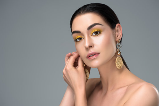 beautiful young woman wearing stylish earrings and looking at camera isolated on grey