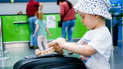 Portrait of 2 years old boy playing with small wooden airplane in airport terminal