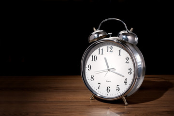 Classic analog alarm clock on wood, dark background with copy space