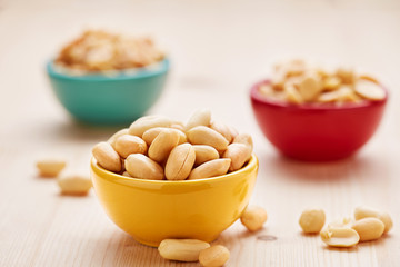 Peanuts bowls on a wooden background. Vegetarian snacks in a colorful bowls. Selective focus.
