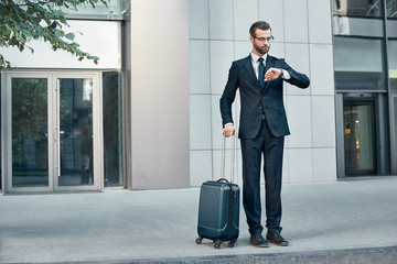 Handsome bearded businessman in classic suit with suitcase is waiting for a taxi