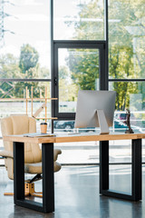 armchair, table with computer, disposable coffee cup and themis statue in business office