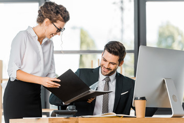 smiling secretary showing folder with documents to handsome businessman in office