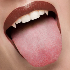 Obraz premium Macro photo of sexy female lips with brown scarlet lipstick. Woman shows her tongue and snow-white teeth with fangs like a vampire. Dentistry, cosmetology, halloween