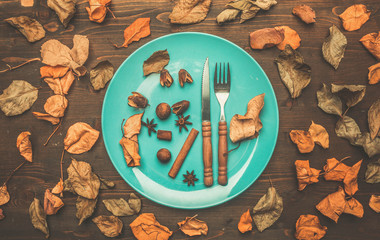 autumn composition, colorful leaves lined around a plate with a knife and fork, nuts, cinnamon and cloves