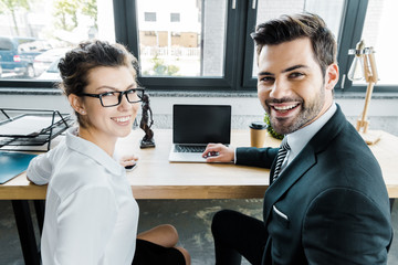 smiling lawyers at workplace with laptop with blank screen and femida in office