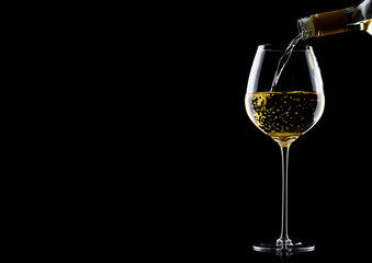 Pouring white wine from bottle to glass on black with space for your text