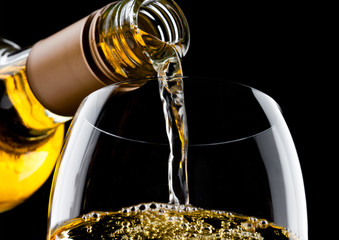 Pouring white wine from bottle to glass on black