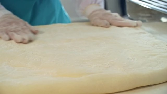 Close up hands of unrecognizable cook wearing gloves and sprinkling flour on dough when making croissants