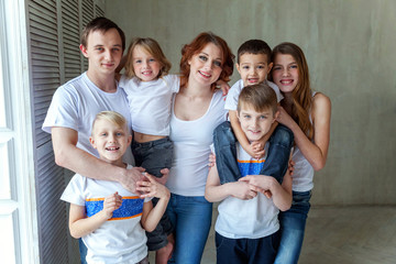 Happy family mother, father and five children near the wall at home. Woman, man and little kids relax in a white bedroom. Happy family at home. Young parents playing whith their children
