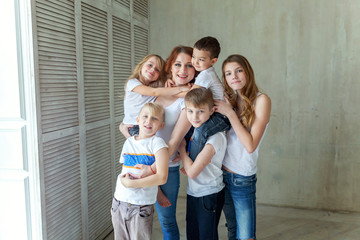 Happy family mother and five children near the wall at home. Woman and little kids relax in a white bedroom. Happy family at home. Young mom playing whith their children