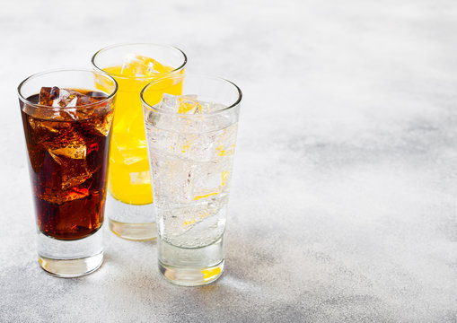 Glasses of soda drink with ice cubes and bubbles on stone kitchen table background. Cola and orange lemonade soda
