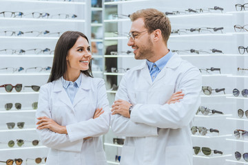 Obraz premium professional smiling doctors posing with crossed arms in ophthalmic shop with eyeglasses