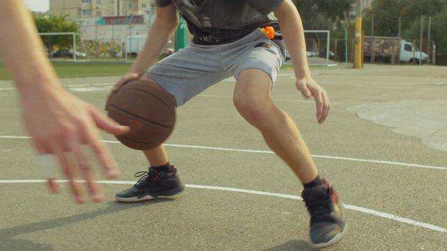 Closeup of male streetball player bouncing the ball and dribbling against defender on bascketball court during game. Low section of basketball player bouncing the ball low to the ground during match.