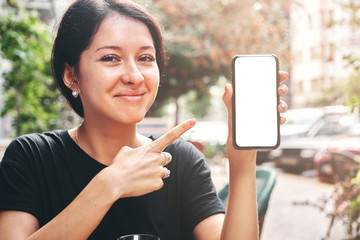 Fototapeta premium Happy beautiful woman holding and showing mobile phone with blank white screen in cafe
