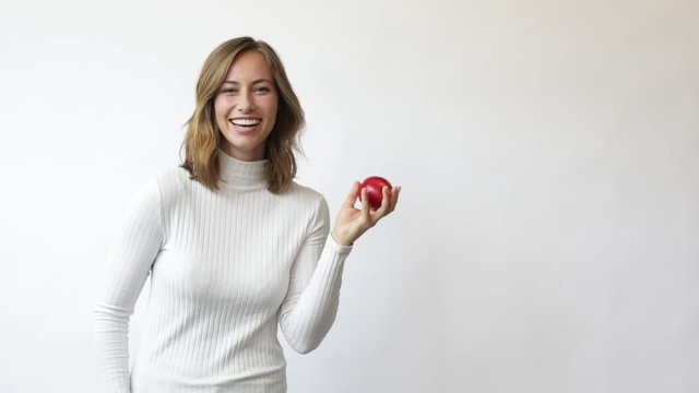 young woman on white background throws red apple up in the air smiling and laughs slowmotion