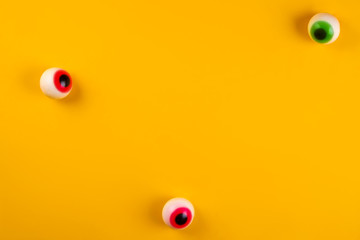 Eyeball shaped candies with red pupils on bright yellow background. Halloween decor concept. Copy...