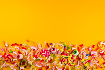 Fototapeta na wymiar Assorted teeth and eyeball shaped candy spread on yellow background, jelly spider, gummy worms, sugar bones, round lollipop and other mixed candy. Top view, copy space, close up, flat lay.