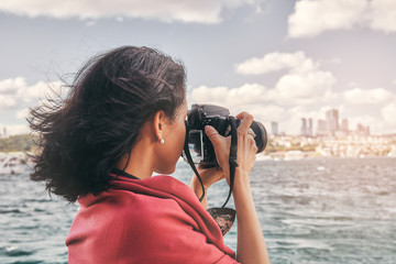 Woman photographer with red scarf, taking pictures of landscape at sea