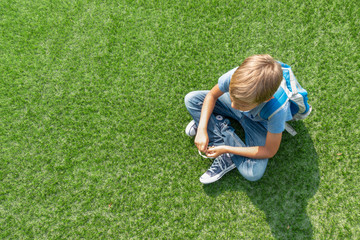 Fototapeta na wymiar Unhappy sad upset boy sitting alone on the grass
