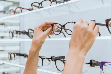 partial view of optician taking glasses from shelf in ophthalmic shop