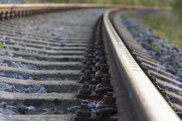 Close-up of the screws on the rail for the train. The sleepers and the two tracks in the distance span into each other.