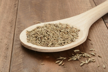 Comino en grano en una cuchara de madera sobre fondo de madera