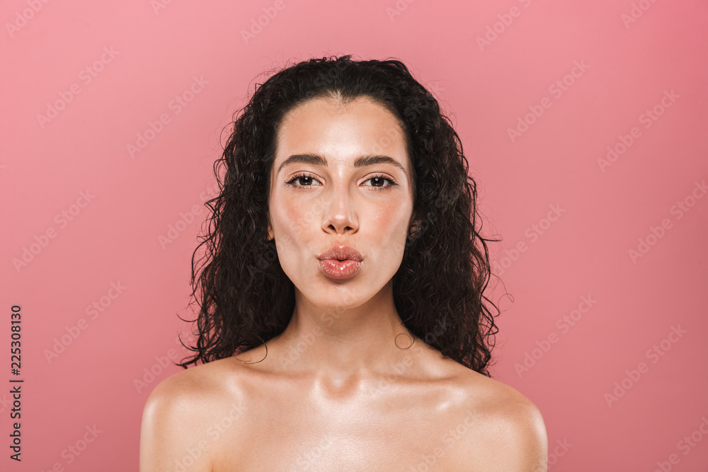 Wall mural Beautiful young woman with healthy skin posing isolated over pink background looking camera.